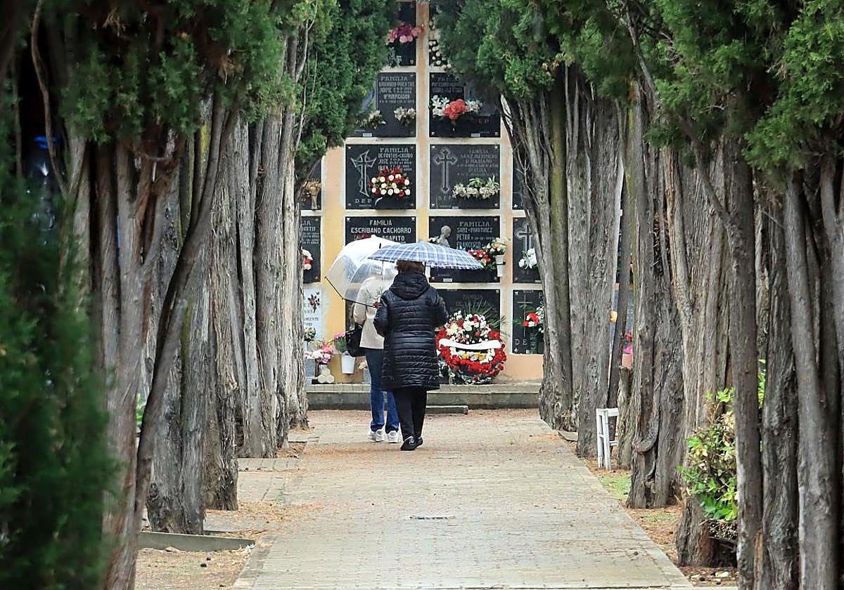 Dos mujeres caminan bajo la lluvia por una de las galerías del cementerio de Segovia.