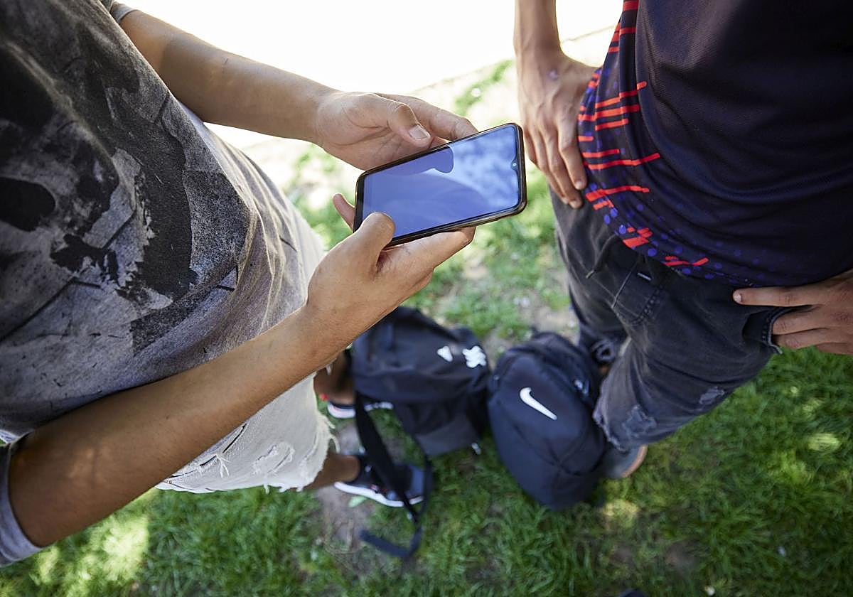 Dos jóvenes manejan un teléfono móvil.