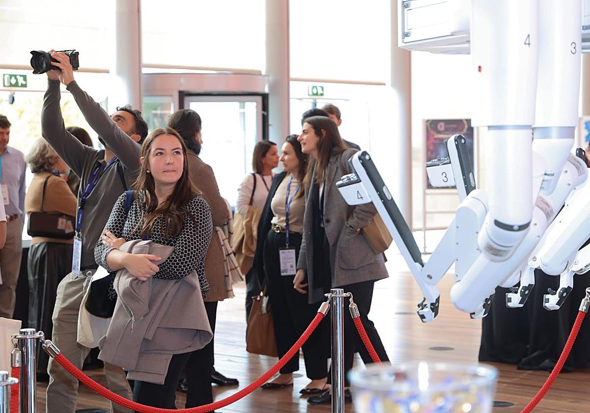 Imagen principal - Una asistente observa el Da Vinci 5. La torre y los cuatro brazos de esta plataforma actualizada y otro de los robots, con cuatro brazos que trabajan por separado de la firma CMR, que pueden ver los cirujanos en la reunión nacional de Valladolid y que utilizan ya profesionales del Ramón y Cajal y Bellvitge.