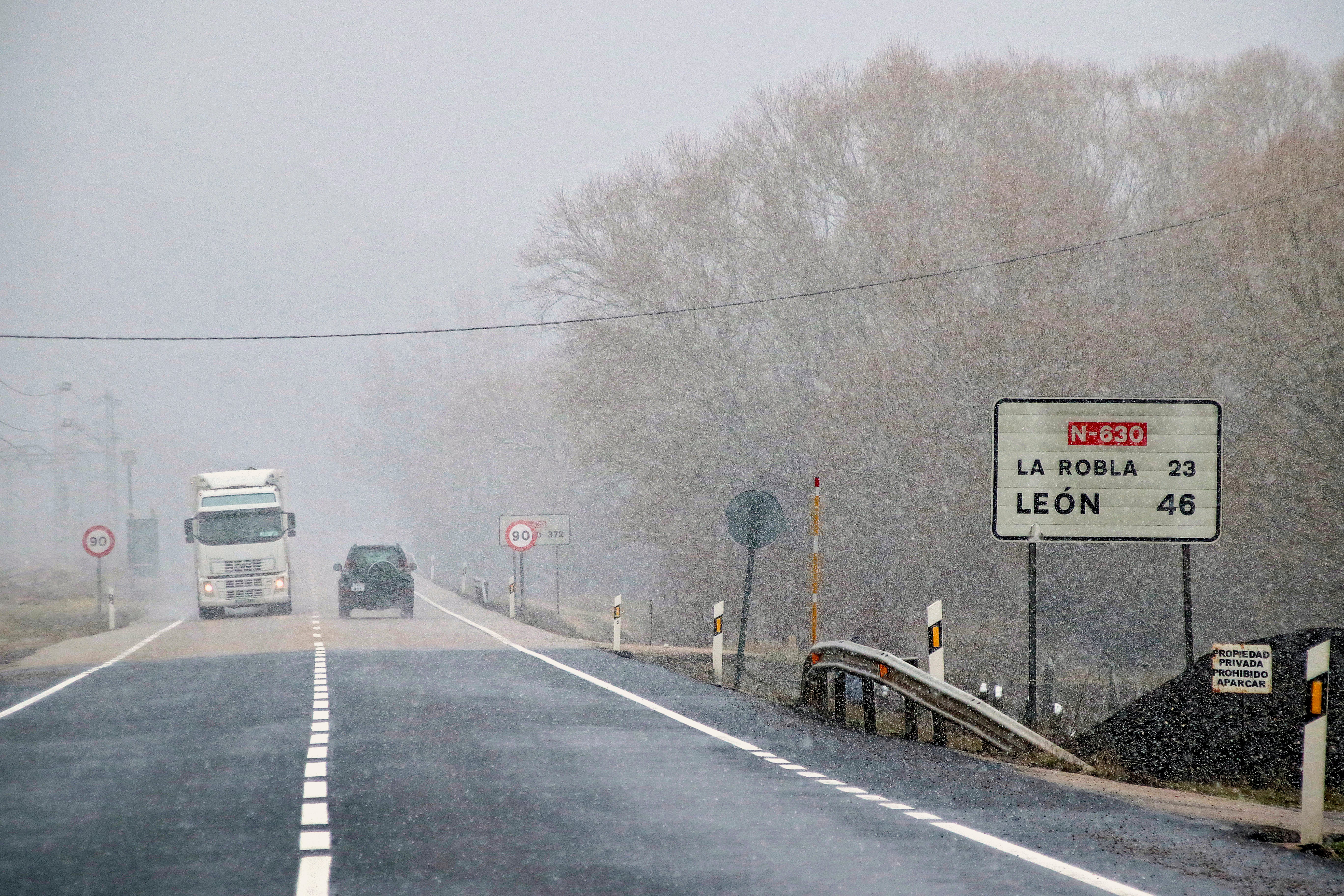 Varios vehículos circulan por una carretera nevada de León.