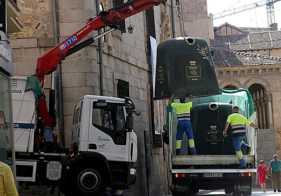 Unos operarios de limpieza recogen unos contenedores en la Calle Real de Segovia.