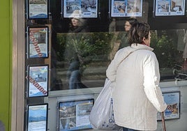 Una mujer camina junto a un escaparate con anuncios de viviendas en venta.