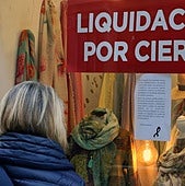 Una mujer se para delante de un escaparate de una tienda de Segovia que anuncia liquidación por cierre.