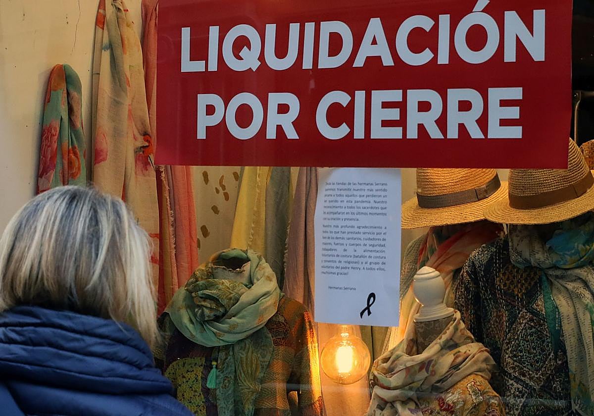 Una mujer se para delante de un escaparate de una tienda de Segovia que anuncia liquidación por cierre.