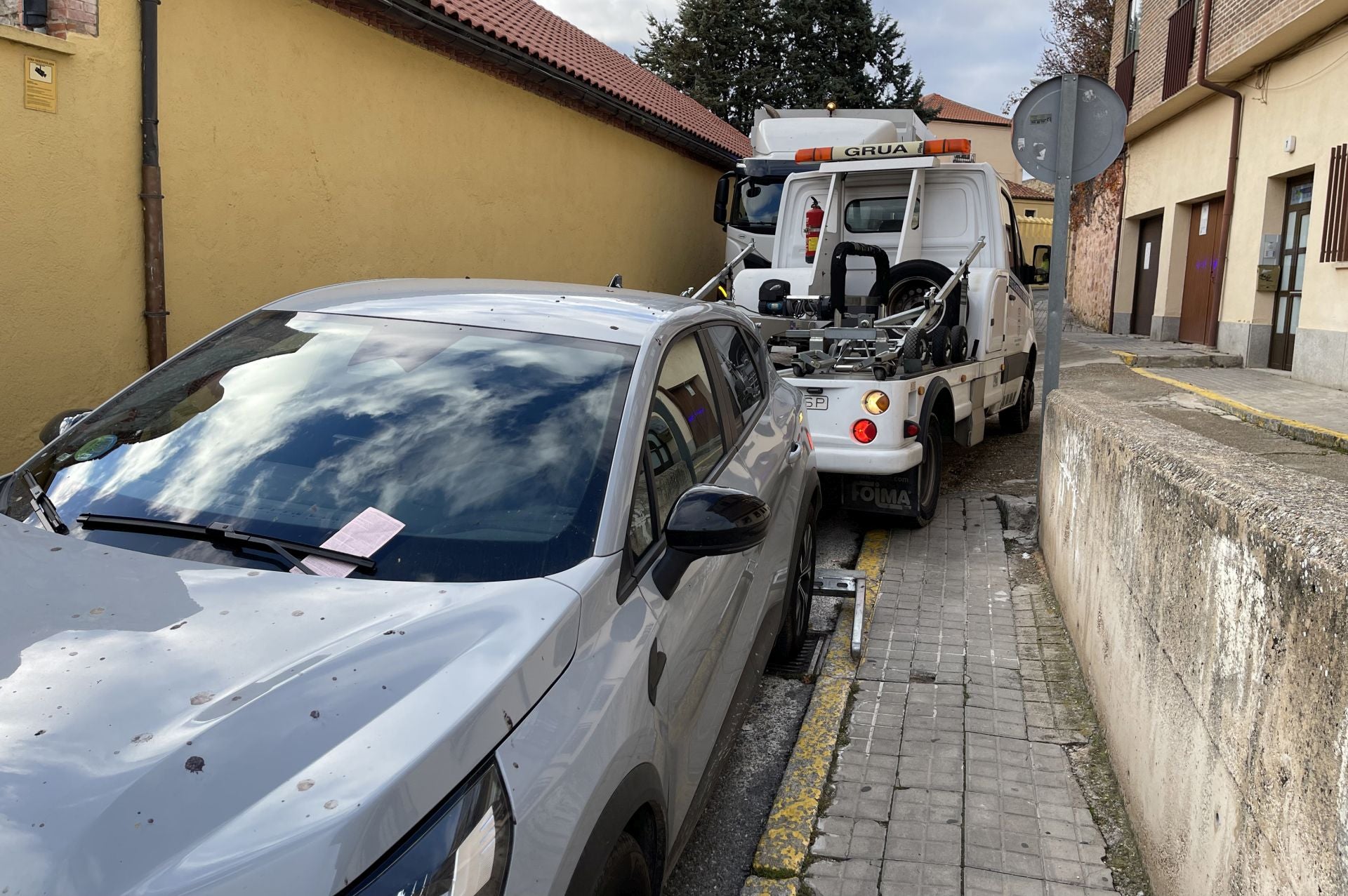 La grúa se lleva el coche mal estacionado que impedía el paso de un camión de la basura.