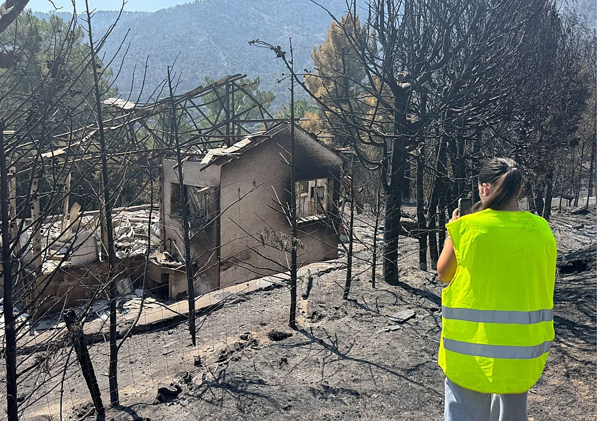 Una mujer fotografía una casa afectada por el incendio en la zona del Embalse del Burguillo, este domingo por la mañana.