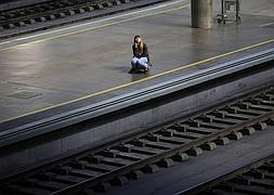 Una mujer espera al tren sentada sobre una maleta en Sevilla. / Marcelo del Pozo (Reuters)