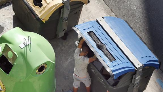 En la imagen, un joven revisa el contenido de un contenedor