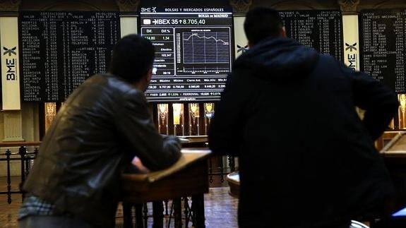 Dos personas observan el panel informativo de la Bolsa de Madrid. 