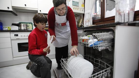 Una mujer y un niño colocan platos en un lavavajillas. 