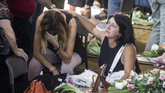 Una mujer reconforta a otra mientras llora ante los ataúdes en el funeral. 