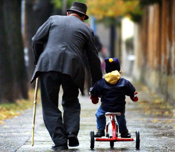 Un abuelo empuja el triciclo que monta su nieto en un parque . 