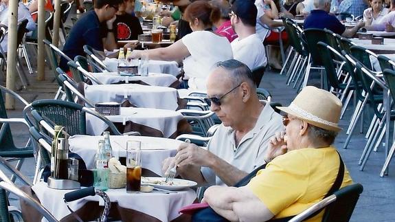 Dos personas disfrutan de la soleada mañana degustando una tapa y un refresco en una terraza de la Plaza Mayor.