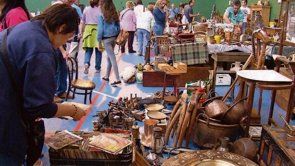 Una asistente a la feria observa un puesto variado y lleno de objetos. 