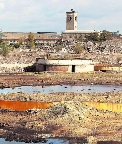 Aspecto de los terrenos, con charcas, escombros, depósitos deteriorados y la iglesia al fondo. 