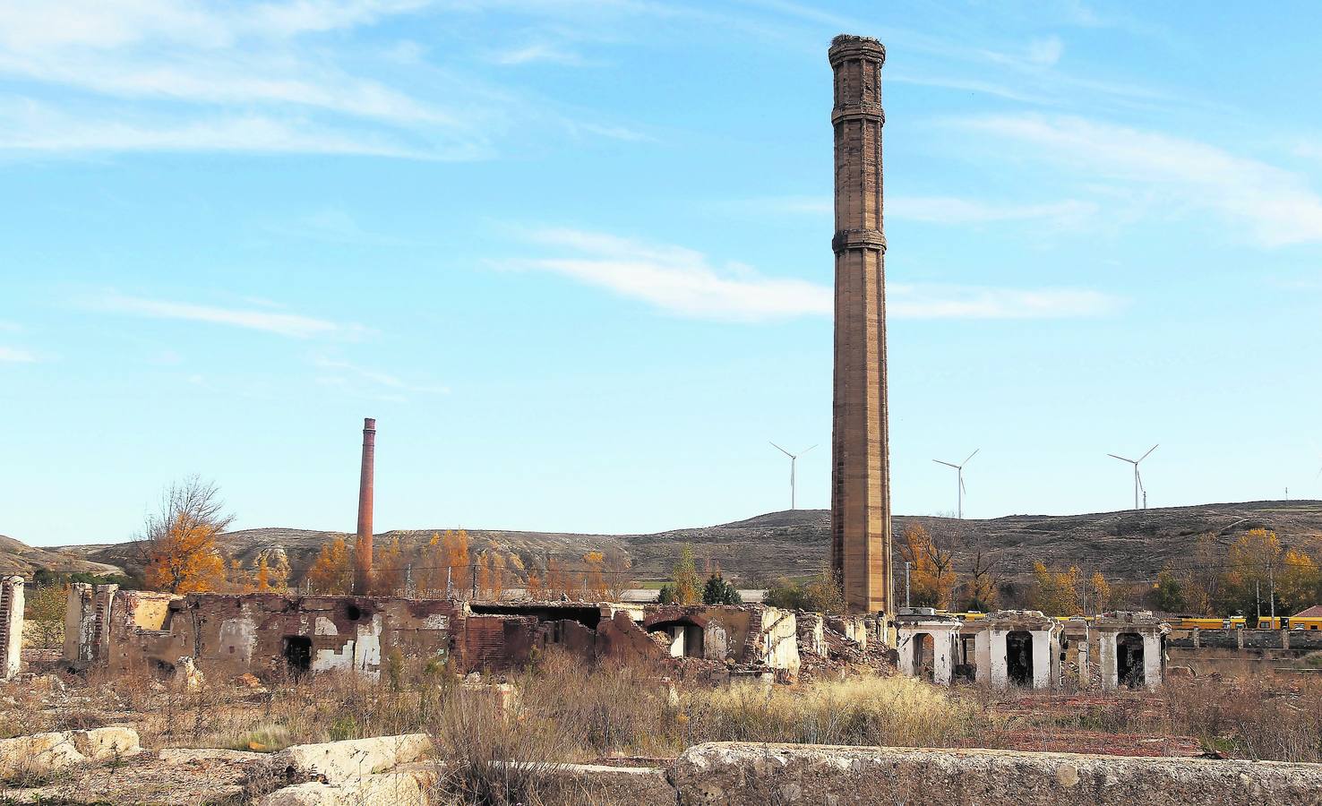 Las chimeneas de la azucarera y de la antigua fábrica de cerámica destacan sobre los edificios derruidos, ante la línea de aerogeneradores eólicos.