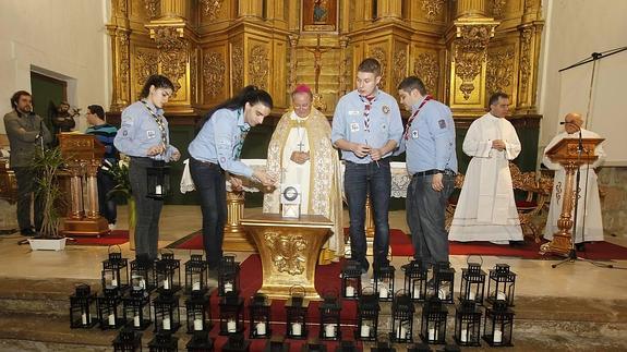 El obispo, ayudado por jóvenes scout, enciende los faroles que entregará a los colectivos.