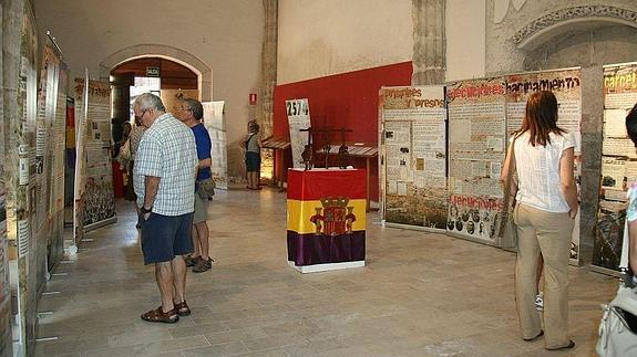 Visitantes de la exposición ‘Tras las rejas’ y, en el centro, monolito que IU quiere instalar en el castillo