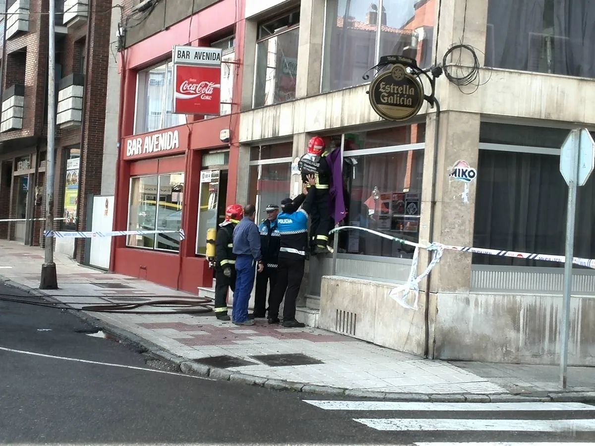 Los bomberos, ayudados por la Policía Local, tratan de acceder al bar. 