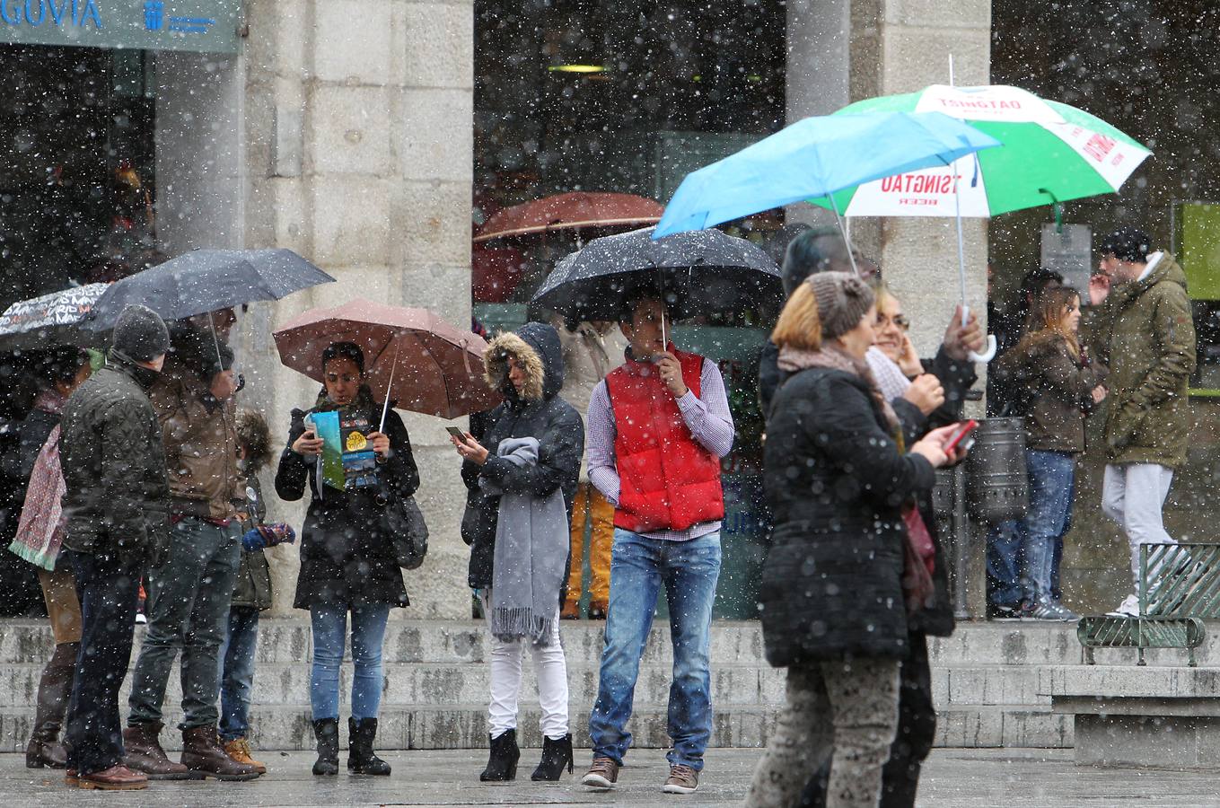 Los transeúntes se protegen de la nevada, este domingo por la mañana, en el Azoguejo de Segovia.
