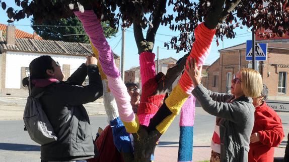 Mujeres de la localidad abrigan con bufandas un árbol.