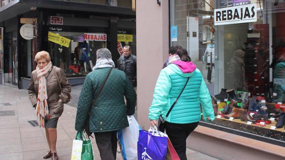 Dos mujeres con bolsas de compras pasan ante escaparates del centro con carteles de rebajas