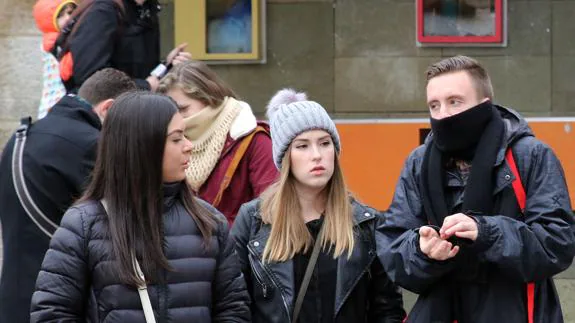 Tres jóvenes se protegen del frío con bufandas y gorros. 