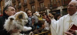Un sacerdote bendice ayer, a las puertas de San Miguel, a varios perros que sostienen en brazos sus propietarios./ FOTOS DE MERCHE DE LA FUENTE