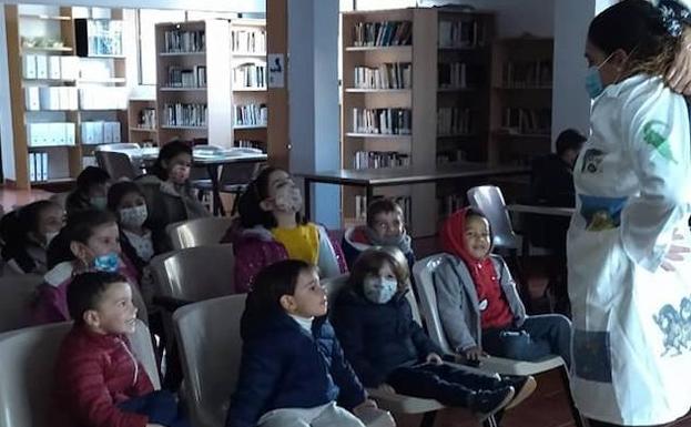 Imagen principal - Arriba, Esther Cordero, responsable de la biblioteca arroyana, contando un cuento. Debajo, los pequeños en una sesión de dibujo tras la lectura.
