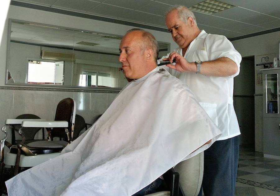 Perche atendiendo a un cliente. Al fondo, uno de los centenarios sillones de la barbería.