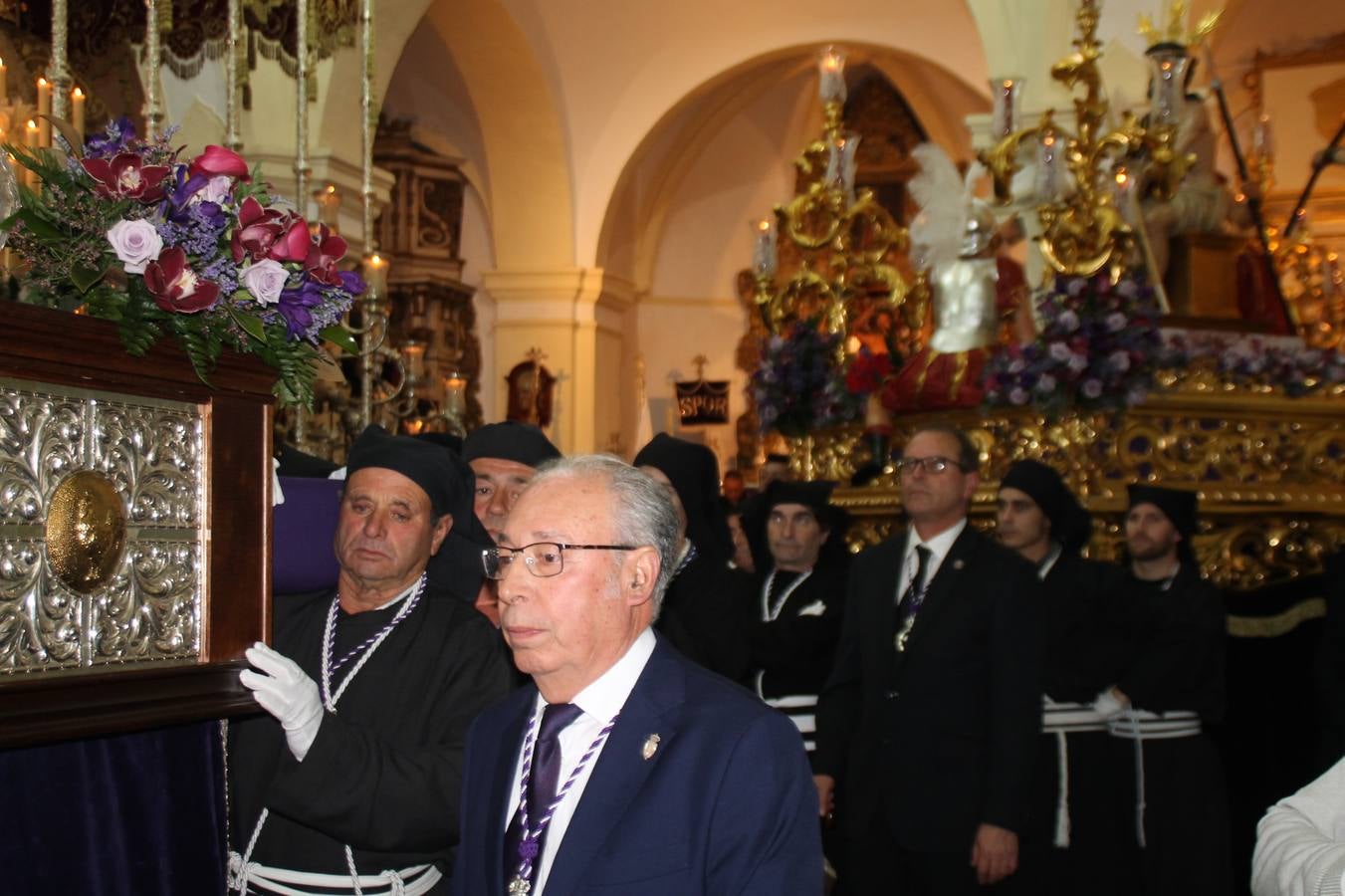Las emociones llenaron también anoche la ermita de Los Santos Mártires, donde se quedaron guardados todos los afanes, las ilusiones y la devoción que no pudieron tener reflejo en la procesión de las colas largas, La Cofradía del Señor Coronado de Espinas decidió no salir ante la adversidad de la climatología y en el interior de este pequeño templo se vivieron momentos de gran emotividad.La Guardia Civil de Jerez de los Caballeros rindió honores a s Madrina, María Santísima de la Amargura. Los sones de las bandas y agrupaciones que iban a participar en el desfile procesional expandieron su eco desde el Llano de los Mártires para acompañar a los costaleros de cada uno de los tres Pasos, que fueron mecidos a su compás. El jovencísimo saetero Julián Jaramillo, de tan solo 12 años y natural de Segura de León, hizo vibrar a los presentes con su saeta al Coronado.Y entre las oraciones del párroco, Antonio María Rejano y los sacerdotes que le acompañaron, asomaron también las lágrimas.El momento más emotivo se vivió con el sentido homenaje a Manuel Labrador González, Manolo 'Cornelio' a quien Marisa Sánchez, en nombre de la junta de gobierno de la Cofradía del Señor Coronado, dedicó palabras llenas de afecto y reconocimiento, destacando su condición de «trabajador sin igual», su carácter innovador, su generosidad, sus consejos a jóvenes y mayores en el seno de esta Cofradía de la que dijo, «es piedra angular» y su extraordinaria labor. Manuel recibió un libro y una precioso cartel realizada por José Tomás Pérez Indiano, a semejanza del que hace tres años anunció la Semana Santa Jerezana. Emocionado, Manuel agradeció el cariño y dedicó este homenaje a su familia y a todas las madres.