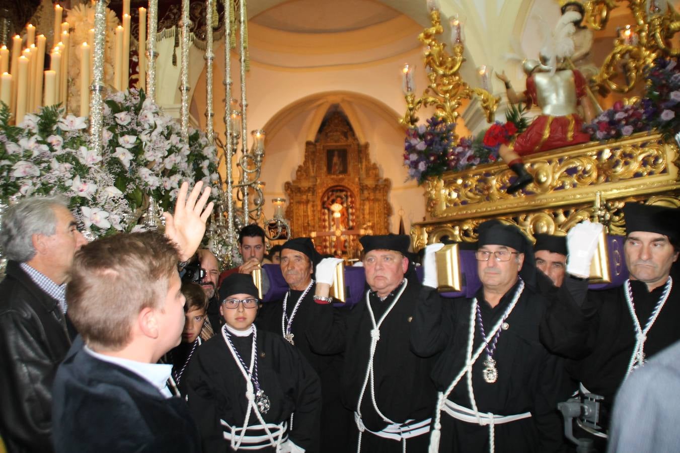 Las emociones llenaron también anoche la ermita de Los Santos Mártires, donde se quedaron guardados todos los afanes, las ilusiones y la devoción que no pudieron tener reflejo en la procesión de las colas largas, La Cofradía del Señor Coronado de Espinas decidió no salir ante la adversidad de la climatología y en el interior de este pequeño templo se vivieron momentos de gran emotividad.La Guardia Civil de Jerez de los Caballeros rindió honores a s Madrina, María Santísima de la Amargura. Los sones de las bandas y agrupaciones que iban a participar en el desfile procesional expandieron su eco desde el Llano de los Mártires para acompañar a los costaleros de cada uno de los tres Pasos, que fueron mecidos a su compás. El jovencísimo saetero Julián Jaramillo, de tan solo 12 años y natural de Segura de León, hizo vibrar a los presentes con su saeta al Coronado.Y entre las oraciones del párroco, Antonio María Rejano y los sacerdotes que le acompañaron, asomaron también las lágrimas.El momento más emotivo se vivió con el sentido homenaje a Manuel Labrador González, Manolo 'Cornelio' a quien Marisa Sánchez, en nombre de la junta de gobierno de la Cofradía del Señor Coronado, dedicó palabras llenas de afecto y reconocimiento, destacando su condición de «trabajador sin igual», su carácter innovador, su generosidad, sus consejos a jóvenes y mayores en el seno de esta Cofradía de la que dijo, «es piedra angular» y su extraordinaria labor. Manuel recibió un libro y una precioso cartel realizada por José Tomás Pérez Indiano, a semejanza del que hace tres años anunció la Semana Santa Jerezana. Emocionado, Manuel agradeció el cariño y dedicó este homenaje a su familia y a todas las madres.