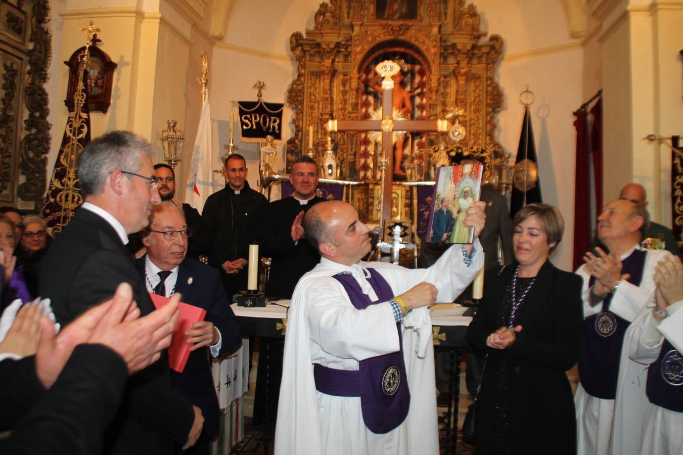 Las emociones llenaron también anoche la ermita de Los Santos Mártires, donde se quedaron guardados todos los afanes, las ilusiones y la devoción que no pudieron tener reflejo en la procesión de las colas largas, La Cofradía del Señor Coronado de Espinas decidió no salir ante la adversidad de la climatología y en el interior de este pequeño templo se vivieron momentos de gran emotividad.La Guardia Civil de Jerez de los Caballeros rindió honores a s Madrina, María Santísima de la Amargura. Los sones de las bandas y agrupaciones que iban a participar en el desfile procesional expandieron su eco desde el Llano de los Mártires para acompañar a los costaleros de cada uno de los tres Pasos, que fueron mecidos a su compás. El jovencísimo saetero Julián Jaramillo, de tan solo 12 años y natural de Segura de León, hizo vibrar a los presentes con su saeta al Coronado.Y entre las oraciones del párroco, Antonio María Rejano y los sacerdotes que le acompañaron, asomaron también las lágrimas.El momento más emotivo se vivió con el sentido homenaje a Manuel Labrador González, Manolo 'Cornelio' a quien Marisa Sánchez, en nombre de la junta de gobierno de la Cofradía del Señor Coronado, dedicó palabras llenas de afecto y reconocimiento, destacando su condición de «trabajador sin igual», su carácter innovador, su generosidad, sus consejos a jóvenes y mayores en el seno de esta Cofradía de la que dijo, «es piedra angular» y su extraordinaria labor. Manuel recibió un libro y una precioso cartel realizada por José Tomás Pérez Indiano, a semejanza del que hace tres años anunció la Semana Santa Jerezana. Emocionado, Manuel agradeció el cariño y dedicó este homenaje a su familia y a todas las madres.