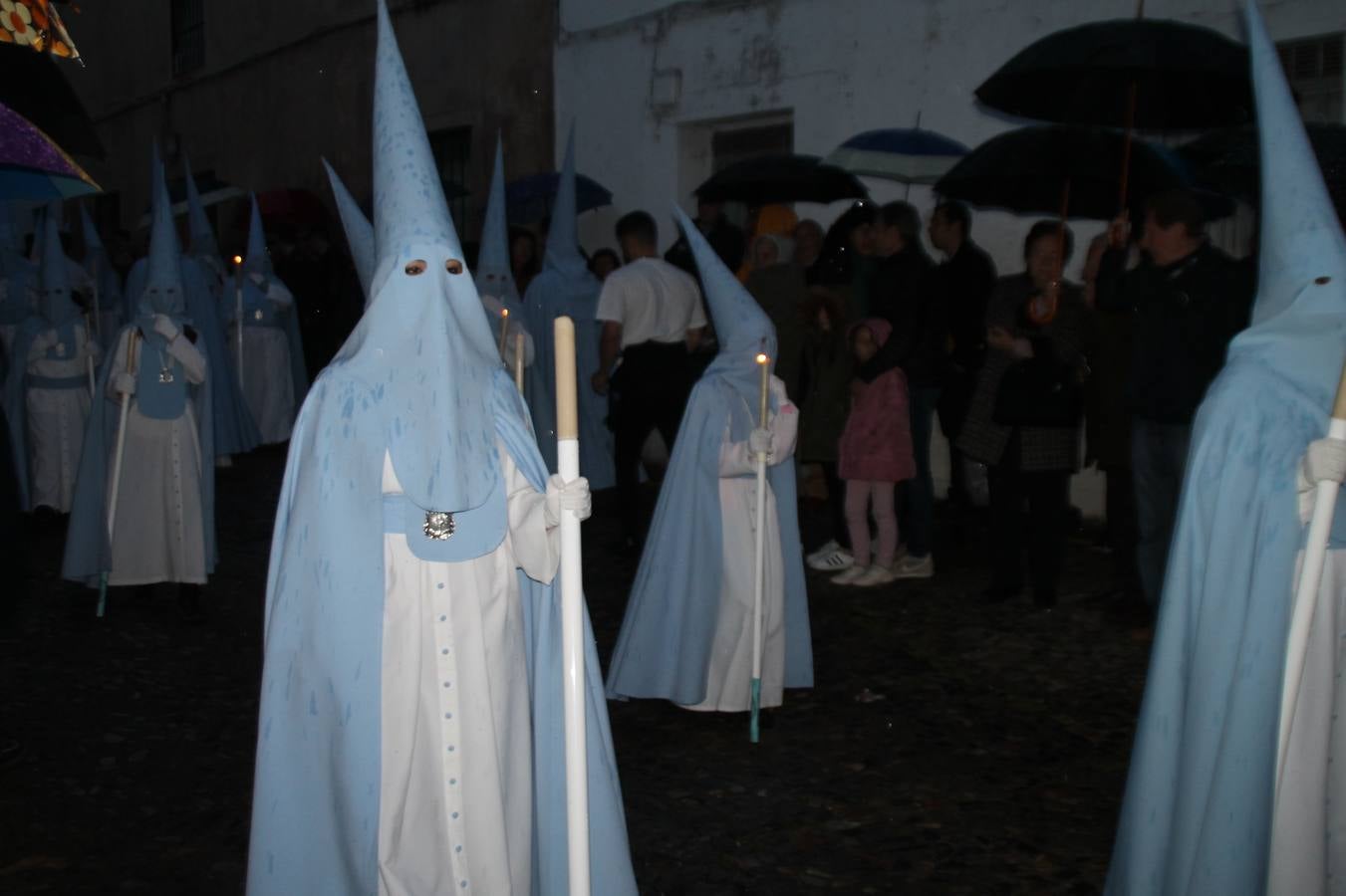 La lluvia que durante las primeras horas de la tarde se contuvo, hizo acto de presencia nada más asomarse a la calle la procesión de las túnicas celestes, que organiza la Archicofrafía del Santísimo Sacramento. Todas las emociones se vieron frustradas y el templo de San Bartolomé fue refugio para el sentimiento de quienes anhelaban acompañar esta estación de penitencia en la que se representa el momento de la institución de la Santa Cena, que junto al de Jesús ante Pilatos, fueron los únicos que realizaron su salida de la iglesia patronal. El Cristo de la Piedad, imagen impresionante en el itinerario de la Semana Santa jerezana, y la hermosa Virgen de la Paza, se quedaron dentro.Los sones de las Agruaciones y bandas que iban a acompañar este desfile sonaron especiales para bailar estas dos imágenes y servir de consuelo, mientras brotaban lágrimas en los ojos de algunos niños que encuentran en esta Cofradía su bautismo nazareno. La oración también acompañó estos momentos de tristeza al tiempo tan especiales.