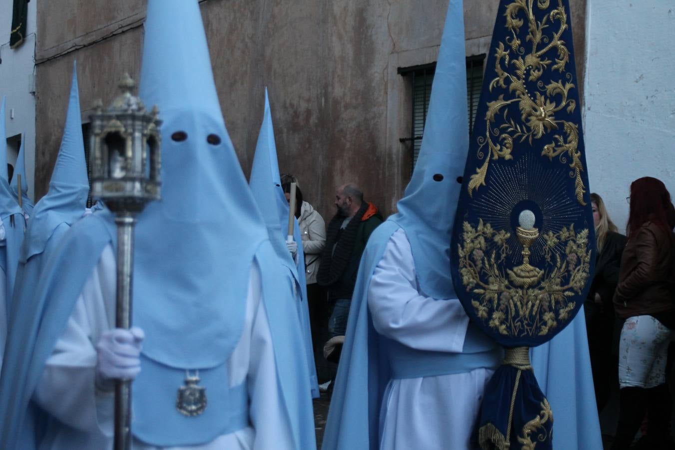 La lluvia que durante las primeras horas de la tarde se contuvo, hizo acto de presencia nada más asomarse a la calle la procesión de las túnicas celestes, que organiza la Archicofrafía del Santísimo Sacramento. Todas las emociones se vieron frustradas y el templo de San Bartolomé fue refugio para el sentimiento de quienes anhelaban acompañar esta estación de penitencia en la que se representa el momento de la institución de la Santa Cena, que junto al de Jesús ante Pilatos, fueron los únicos que realizaron su salida de la iglesia patronal. El Cristo de la Piedad, imagen impresionante en el itinerario de la Semana Santa jerezana, y la hermosa Virgen de la Paza, se quedaron dentro.Los sones de las Agruaciones y bandas que iban a acompañar este desfile sonaron especiales para bailar estas dos imágenes y servir de consuelo, mientras brotaban lágrimas en los ojos de algunos niños que encuentran en esta Cofradía su bautismo nazareno. La oración también acompañó estos momentos de tristeza al tiempo tan especiales.