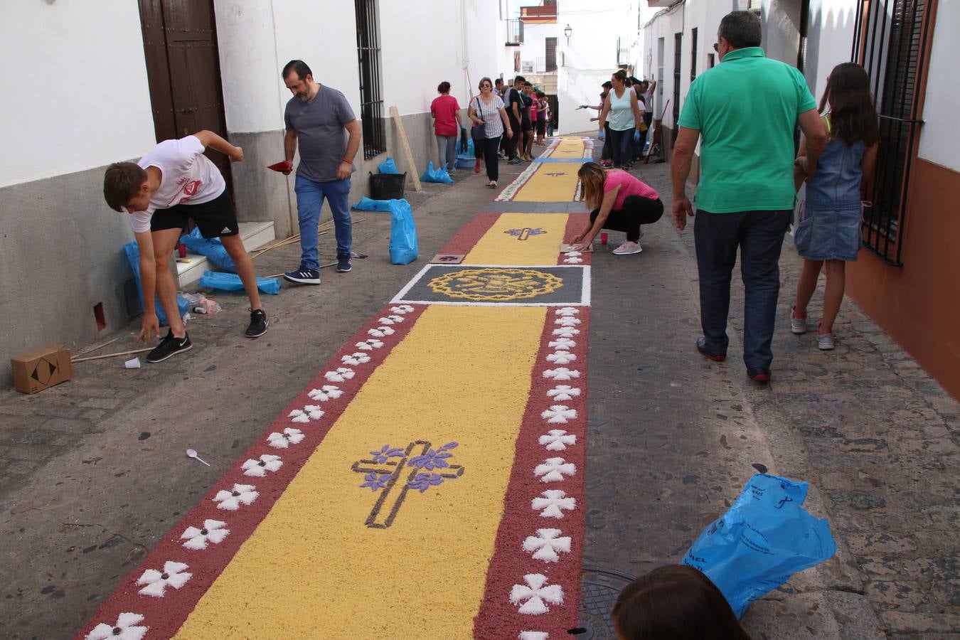 Las alfombras de sal embellecen y llenan de color, hoy, las calles de Jerez de los Caballeros con motivo de la festividad del Corpus Christi. Desde primera hora de la mañana, miembros de las cofradías y hermandades, Cáritas, grupos de catequesis, familias de los niños que han hecho este año la Primera Comunión, miembros de la Asociación de costaleros y costaleras de la Semana Santa jerezana, Ayuntamiento y vecinos han cubierto las principales calles del municipio con 6.250 kilos de sal teñida, plenas de color. A continuación, han disfrutado de una jornada de convivencia en la Casa de la Iglesia 'Cecilia de Arteaga'.