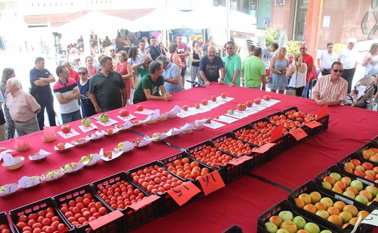 Varias personas se agolpan junto a un puesto de exposición de tomates 