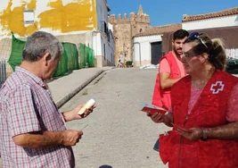 Dos voluntarios informan a un vecino y entregan un bote de protección solar.