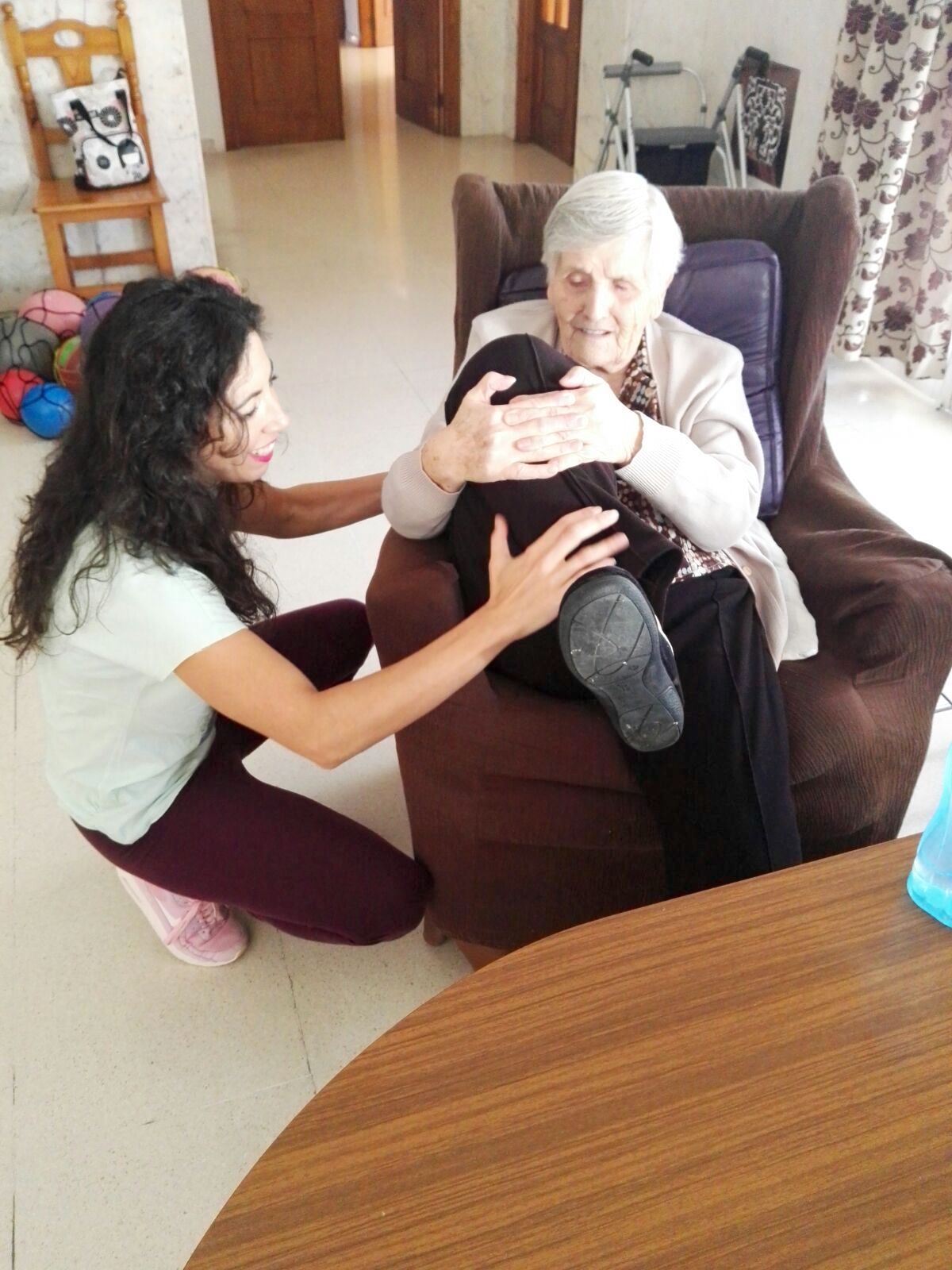 Una abuela mueve su pierna con ayuda de la monitora 