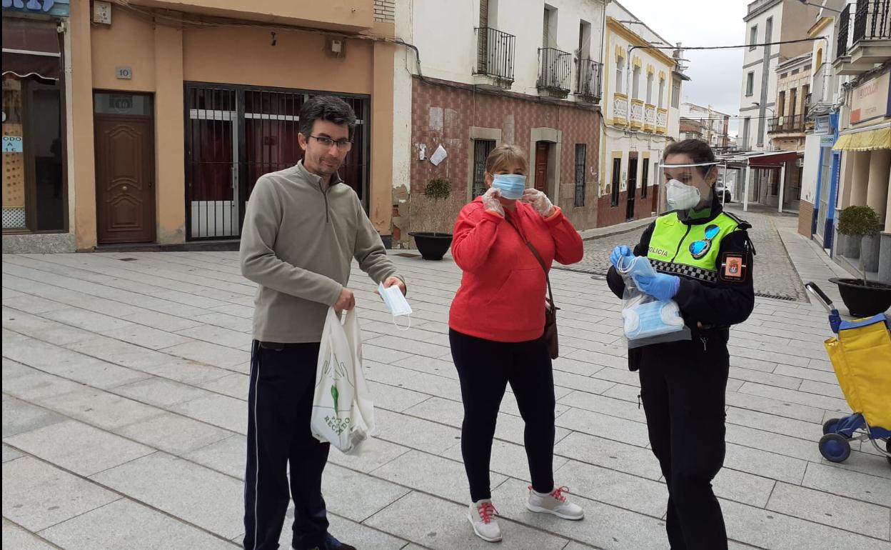 Una agente de la Policía Local hace entrega de mascarillas a dos vecinos en la Plaza de España 