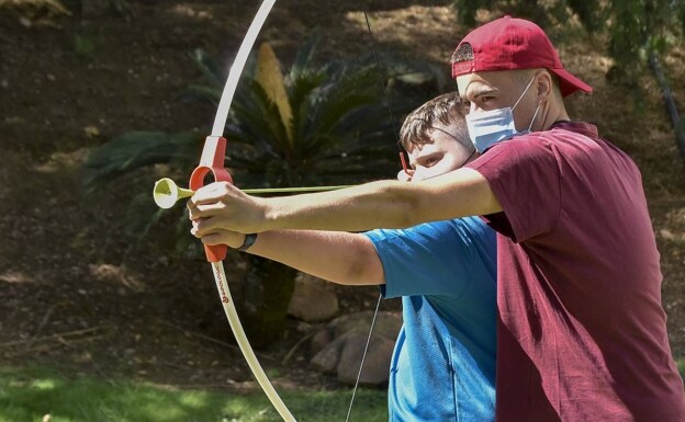 Uno de los monitores enseña a un participante en los respiros de Plena Inclusión a hacer tiro con arco. 