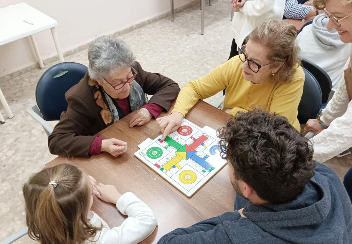 Mayores y pequeños juegan al parchís.
