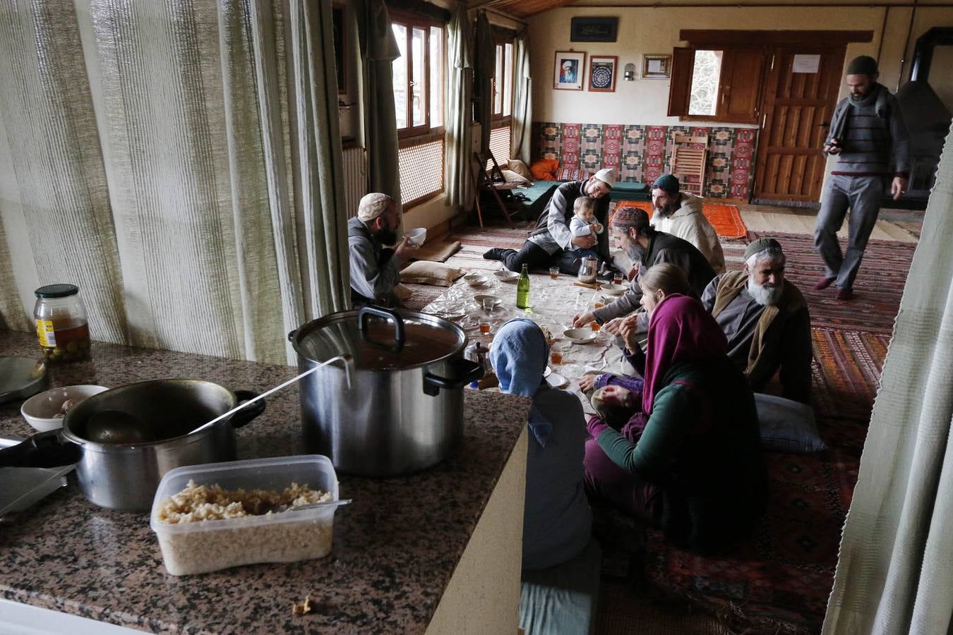 Las mujeres comparten una mesa. Al lado, los hombres en otra, con la comida servida sobre un mantel en el suelo