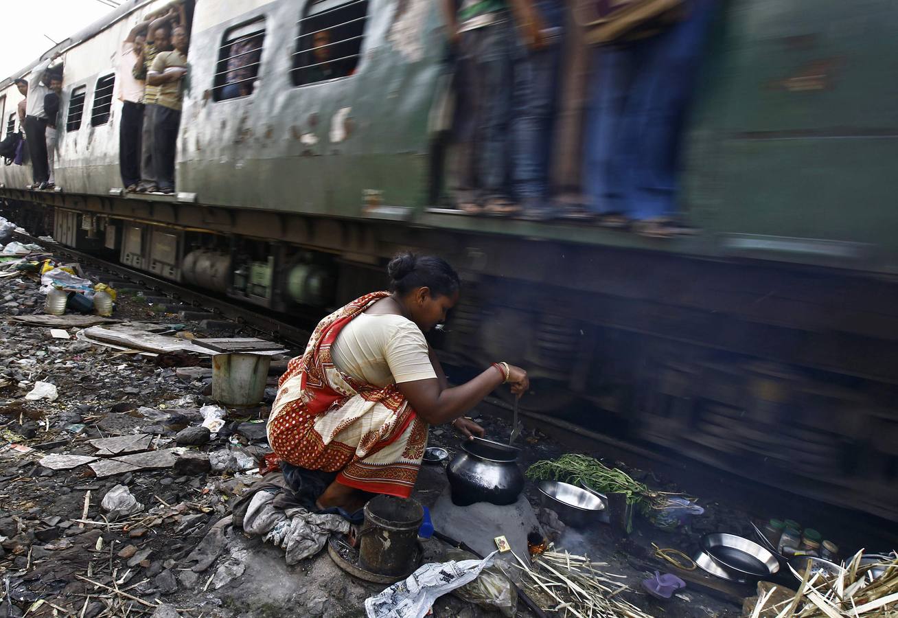 Una mujer cocina a pocos centímetros de las vías de la estación de tren cerca de Calcuta