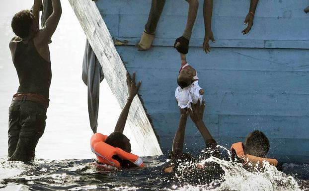 Grupo de inmigrantes en aguas del Mediterráneo suben a un bebé a la embarcación de rescate. 