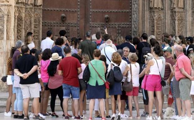 Un gran númeo de turistas contempla la puerta de los Apóstoles en la plaza de la Virgen, en Valencia. 