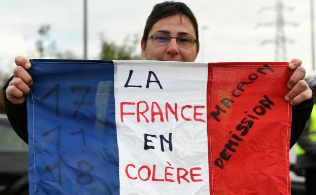 Una mujer sostiene una bandera francesa que dice «Francia en cólera, abdicación de Macron».