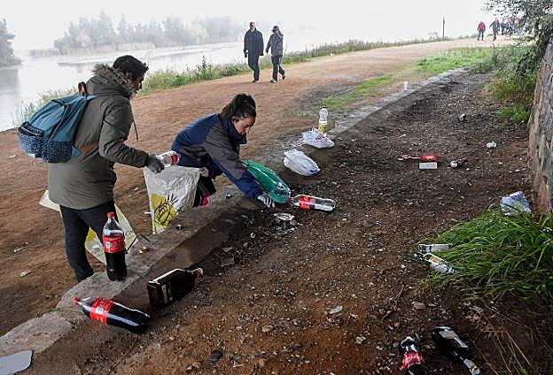 Dos voluntarias recogen restos de botellón bajo el Puente Real. 