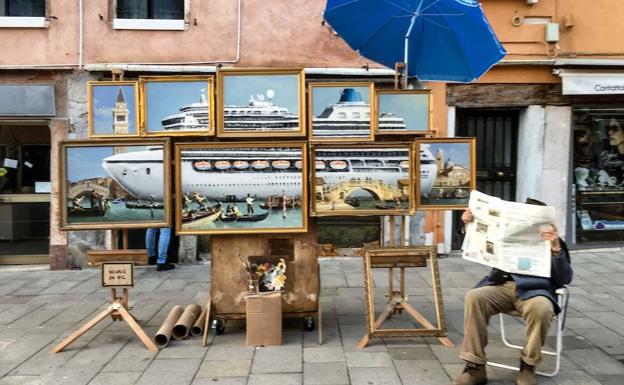 Un hombre anónimo, que se supone que es el artista de la calle británico Banksy, se sienta junto a un montaje de pinturas al óleo titulado «Venice in oil».