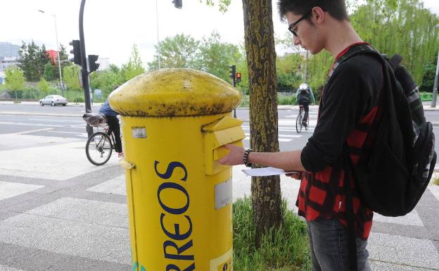 Un joven mete una carta en un buzón de Correos.